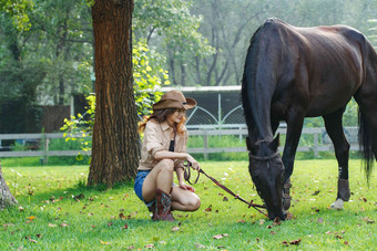户外青年女人看着马儿吃草