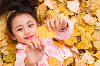 快乐的小女孩躺在落叶上玩耍
