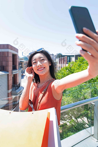 户外挎着购物袋拿手机自拍的青年女人