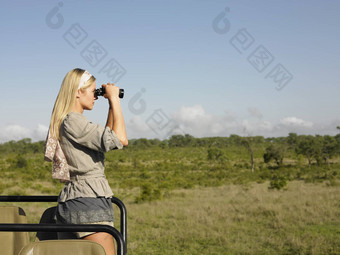 一边视图年轻的金发碧眼的女人Safari站吉普车双筒望远镜