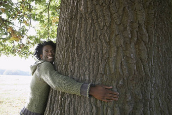快乐年轻的非洲美国男人。拥抱树树干公园