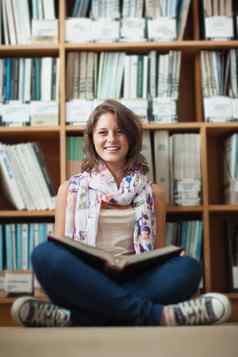 微笑女学生书架上阅读书图书馆地板上