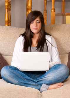 年轻的女人移动PC可移植的电脑坐着沙发