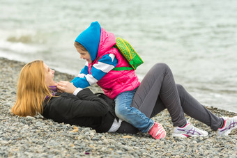 五年女孩温暖的衣服坐在两腿分开着妈妈。说谎卵石海滩海有趣的