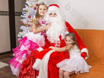 女孩美丽的礼服拥抱圣诞老人老人坐着沙发上