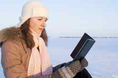 青少年女孩阅读电子书在户外冬天时间