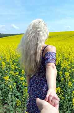 遵循金发女郎女孩衣服花打印盛开的黄色的油菜籽场
