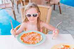 肖像可爱的女孩坐着晚餐表格吃披萨