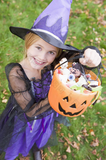 年轻的女孩在户外女巫服装万圣节持有糖果
