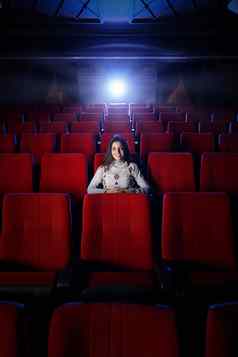 美丽的年轻的女人坐着空电影剧院