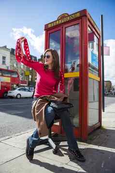 年轻的女人挥舞着伦敦红色的电话展位回来