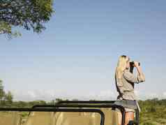 后视图年轻的金发碧眼的女人Safari站吉普车双筒望远镜