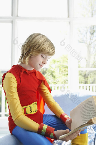 年轻的男孩超人服装阅读书在室内