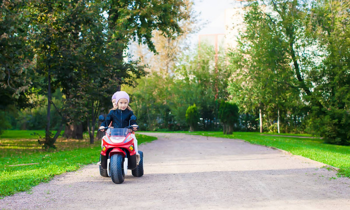 可爱的女孩骑儿童摩托车绿色公园