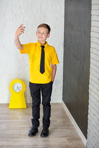可爱的英俊的学校男孩黄色的t恤领带时尚的靴子casuals站陈词滥调黑色的董事会数字持有聪明的电话微笑
