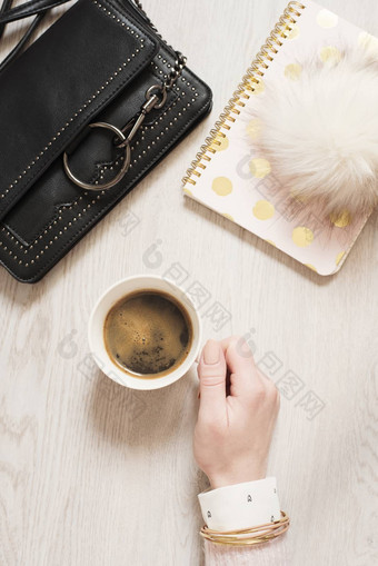 前视图女人手持有杯黑色的咖啡平躺工作空间笔记本粉红色的黄金时尚手提包皮毛球