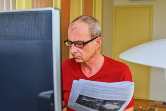 中间岁的男人。眼镜坐着桌子上成熟的男人。个人电脑高级概念男人。文书工作沉思的男人。工作首页办公室