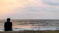 模糊图像孤独的男人。坐着海滩日落时间后视图孤独的思考人荒野区域休息放松休闲活动背景概念