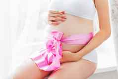 怀孕了女人白色内衣粉红色的弓肚子年轻的女人期待婴儿女孩舒适的快乐背景阳光明媚的早....