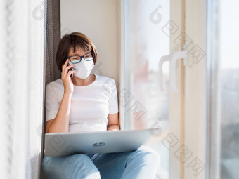 女人医疗面具远程作品首页坐在窗口窗台上智能手机移动PC膝盖封锁检疫冠状病毒科维德隔离首页