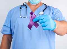 医生蓝色的统一的乳胶手套持有紫色的丝带