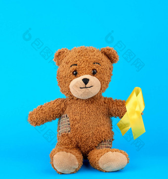 棕色（的）泰迪熊坐在持有爪子<strong>黄色</strong>的丝绸<strong>丝带</strong>