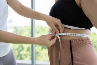 年轻的女教练测量脂肪层超重女人腰围健身
