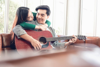 年轻的夫妇爱放松沙发生活房间玩吉他享受唱首歌首页浪漫的亚洲夫妇放松享受休闲活动首页保持首页