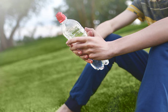 年轻的高加索人男人。跑步者放松持有喝水瓶坐着草公园在户外体育运动早期早....时间锻炼健康的概念