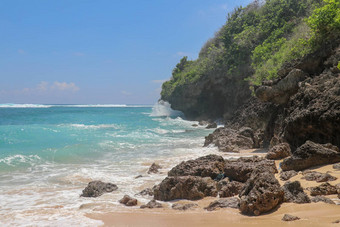 海滩山伞海滩细金沙子巴厘岛绿松石蓝色的水转海泡沫波打破岩石悬崖海岸阳光明媚的一天蓝色的天空旅游自然概念