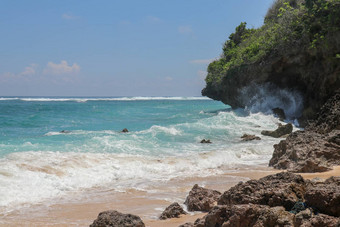海滩山伞海滩细金沙子巴厘岛绿松石蓝色的水转海泡沫波打破岩石悬崖海岸阳光明媚的一天蓝色的天空旅游自然概念
