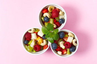 新鲜的水果沙拉白色碗混合水果白色碗健康的食物风格水果沙拉新鲜的水果浆果粉红色的背景碗水果沙拉