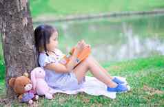 可爱的女孩阅读书娃娃公园