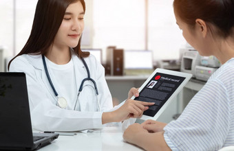 亚洲女人医生持有平板电脑病人医疗记录屏幕咨询病人医疗咨询房间