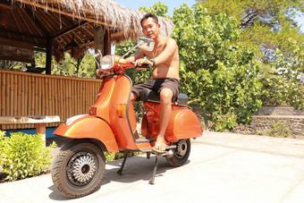 巴厘岛印尼7月尤格风印尼男人。坐着橙色经典维斯帕橙色经典维斯帕橙色维斯帕超级摩托车停人行道上