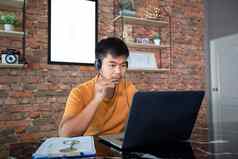 亚洲商人笔记本电脑穿耳机在线会议工作首页