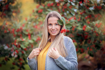 年轻的女孩灰色的针织毛衣走秋天公园红色的浆果