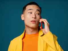 男人。移动电话手黄色的夹克橙色毛衣蓝色的背景