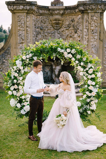 新郎把环新娘手指婚礼酒庄别墅托斯卡纳意大利轮婚礼拱装饰白色花绿色植物前面古老的意大利体系结构