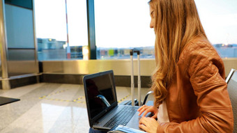 休闲女人工作移动PC机场大厅女人等待飞行机场终端坐着椅子打字移动PC