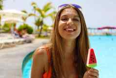 微笑美丽的女孩吃冰棒冰流行形式西瓜片相机夏天假期概念