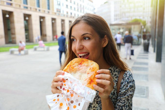 快乐年轻的业务女人吃小披萨短午餐打破城市女孩吃传统的意大利披萨米兰主要街意大利披萨情人概念