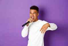 图像时髦的非裔美国人的家伙唱歌麦克风说唱执行阶段站紫色的背景