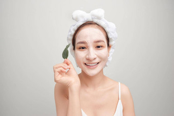 亚洲女人毛巾应用白色面部粘土面具持有叶