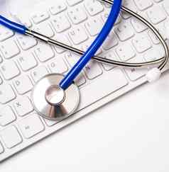 蓝色的听诊器电脑键盘白色表格背景在线医疗信息治疗技术概念关闭宏复制空间