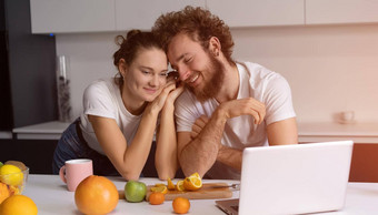 美丽的年轻的夫妇会说话的视频调用移动PC年轻的夫妇烹饪健康的食物厨房首页男人。靠女孩微笑看浪漫的电影