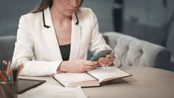 关闭美丽的办公室工人白色夹克使笔记杂志持有智能手机电话手坐着前面杂志办公室工人工作的地方