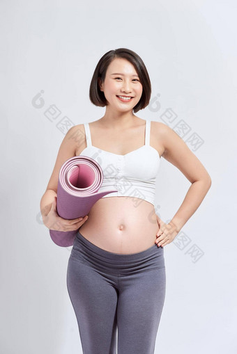 年轻的有吸引力的怀孕了女触碰肚子持有瑜伽席手准妈妈。<strong>物理</strong>练习摆姿势孤立的白色<strong>背景</strong>