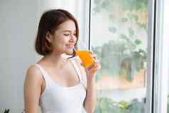 漂亮的年轻的亚洲女人明亮的房间喝橙色汁