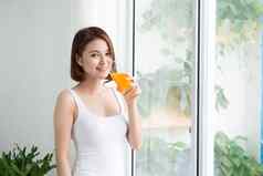 漂亮的年轻的亚洲女人明亮的房间喝橙色汁